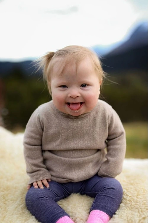 Toddler with an open-mouth grin, wearing a tan sweater and dark blue leggings.