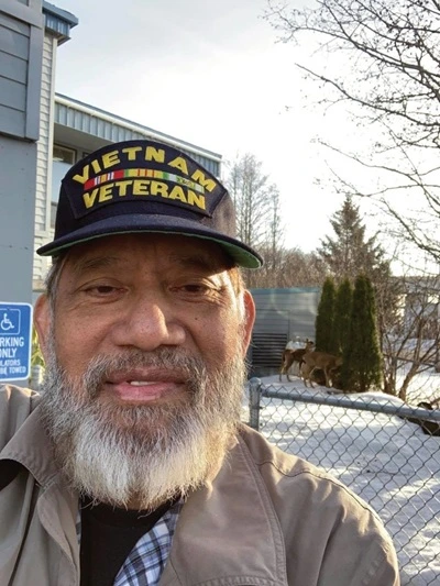 Man with a gray beard, wearing a Vietnam Veteran baseball cap. He is in front of a snow-covered yard.