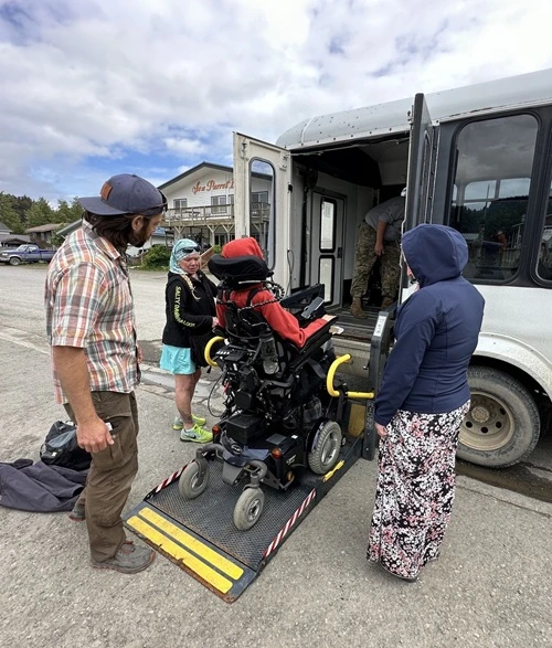 Person in a wheelchair being assisted onto a ramp of a van.