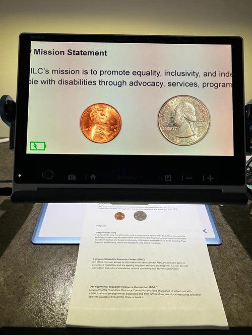 A magnifying device showing a large, close-up view of a piece of paper with the ILC's mission statement and two coins.