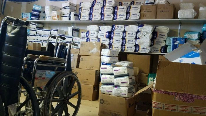 Inventory of medical supplies, including numerous packages of adult diapers, and wheelchairs, stored on shelves and in boxes.