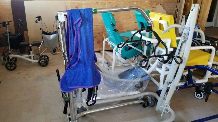 Assorted medical equipment, including wheelchairs, walkers, and a transfer lift, stored in a room.