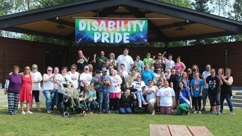 Large group of people under a colorful banner that reads 'Disability Pride'.